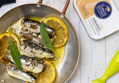 foto de uma receita de sardinhas com rodelas de limão em uma panela e uma lata de sardinha em conserva gourmet da La Compagnie Bretonne, fornecedora parceira da Fui ao Mar no Brasil